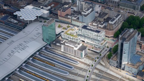 Aerial view of a modern urban area with a train station, surrounding buildings, and green spaces.