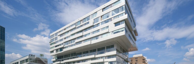 A modern, angular white building with large windows set against a blue sky with clouds.