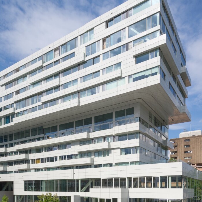 A modern, angular white building with large windows set against a blue sky with clouds.