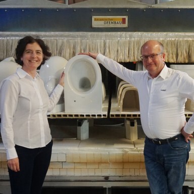 Zwei Personen stehen in einer Fabrikhalle vor einer Maschine, die Keramiken für Toilettenformen brennt.