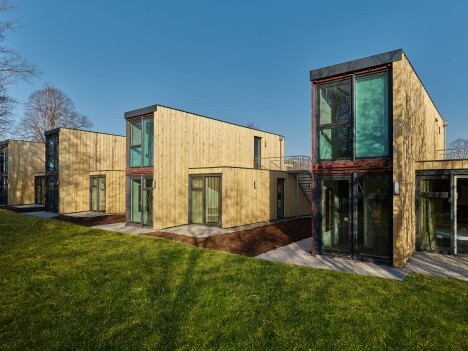 Moderne Holzhäuser mit grossen Fenstern und grüner Wiese bei klarem Himmel.