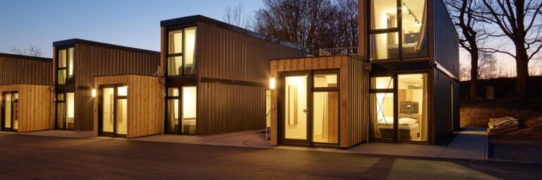 Moderne Wohngebäude aus Holz mit grossen Fensterflächen bei Dämmerung.