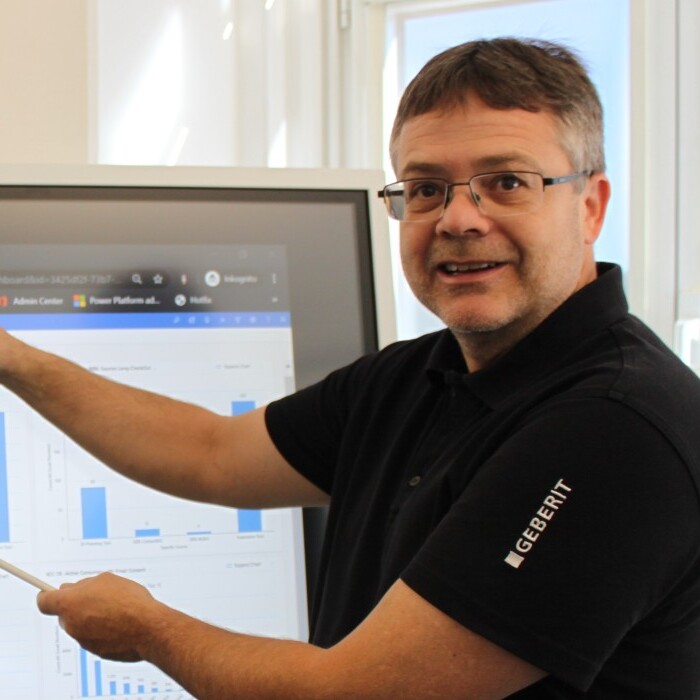 Ein Mann präsentiert Grafiken und Daten auf einem grossen Bildschirm in einem modernen Büro.