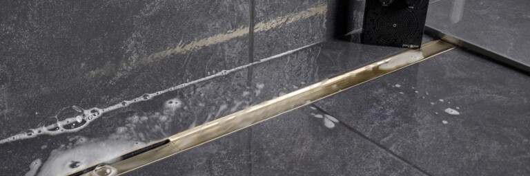 A close-up of a tiled floor showing a metallic linear drain and water residue.