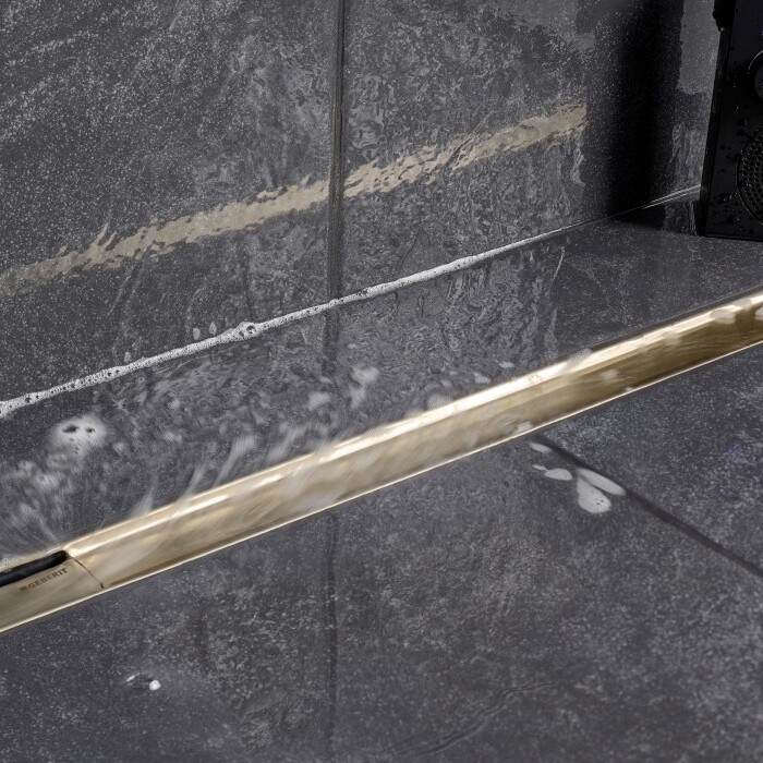 A close-up of a tiled floor showing a metallic linear drain and water residue.