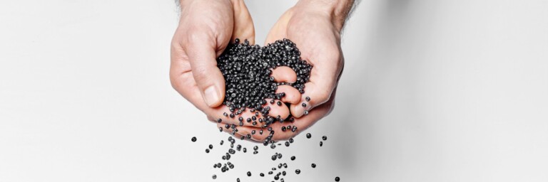 Two hands are cupping and releasing small black balls against a white background.