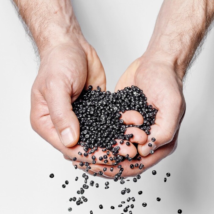 Two hands are cupping and releasing small black balls against a white background.