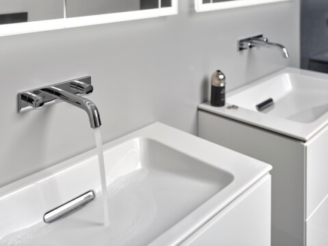 A modern bathroom with two white sinks, chrome faucets and a minimalistic design, one with running water.