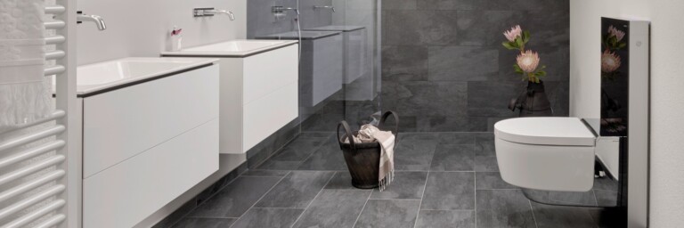 Spacious modern bathroom with gray tiled floor, white cabinetry, two sinks, and a minimalist toilet.