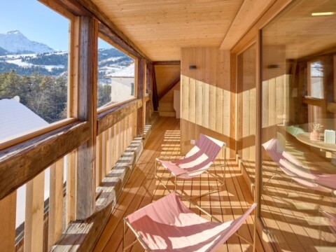 Holzbalkon mit zwei Liegestühlen und Blick auf die Berge, helle Holzverkleidung und grosse Fenster.