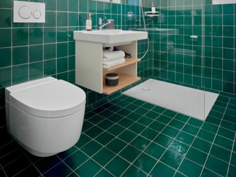 Modernes Badezimmer mit grünen Fliesen, Wandtoilette, Waschbecken und offener Dusche.