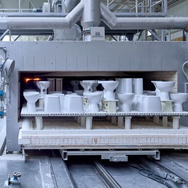 A manufacturing machine in a factory setting displaying several white toilet bowls on a conveyor system.