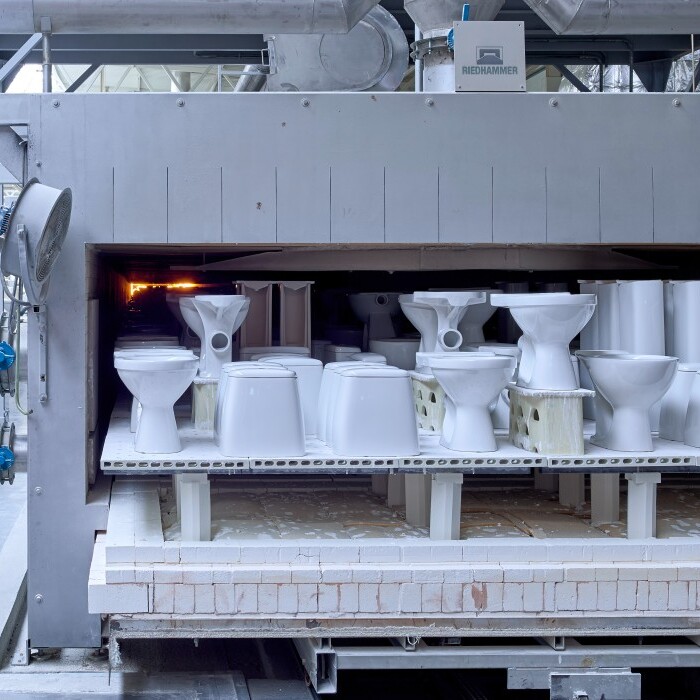 An industrial facility showing a large kiln or drying chamber with white ceramic toilets stacked inside.