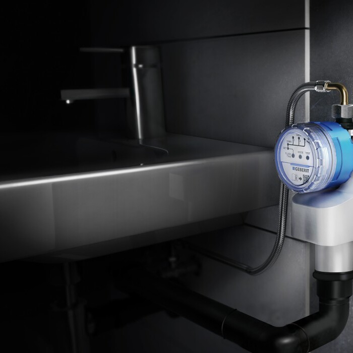 A close-up view of a water meter installed beside a sink, with dark surroundings and visible plumbing.
