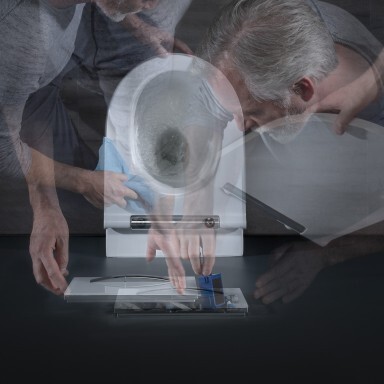 A person with gray hair is bending over a toilet while inspecting or cleaning it, surrounded by a blurred background.