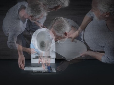 A blurred image showing an older person bending over a toilet, with multiple overlapping views of their head and hands engaged in some action.