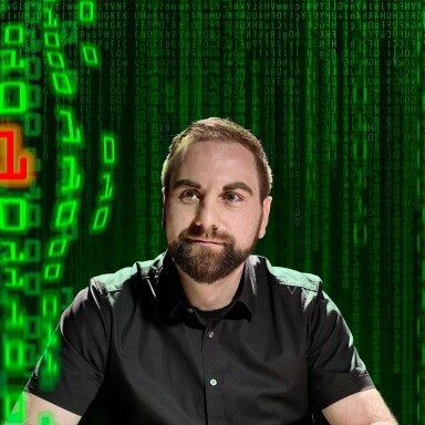 A man with a beard sits in front of a keyboard, with a green binary code background.