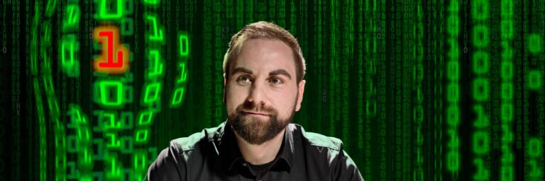 A man with a beard sits in front of a green digital background with zeros and ones.