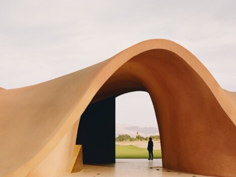 Eine skulpturale, geschwungene Architektur öffnet sich zu einem weiten Blick ins Freie, mit einer Person, die darunter steht.