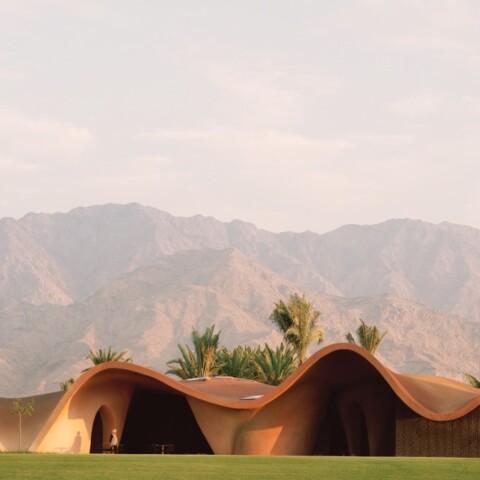 Eine moderne Architektur mit wellenförmigem Dach, umgeben von Palmen und hinterlegt mit Bergen im Hintergrund.