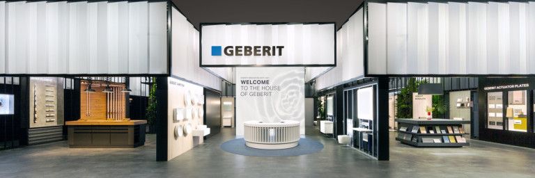 A modern exhibition space featuring Geberit signage, with booths displaying various products and a central welcoming area.