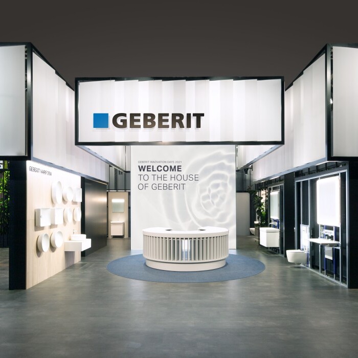 A modern exhibition space featuring Geberit signage, with booths displaying various products and a central welcoming area.