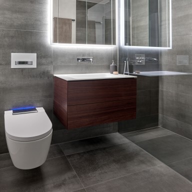 Moderne Badezimmeransicht mit einem hängenden Waschtisch, einem beleuchteten Spiegel und einem weissen WC.