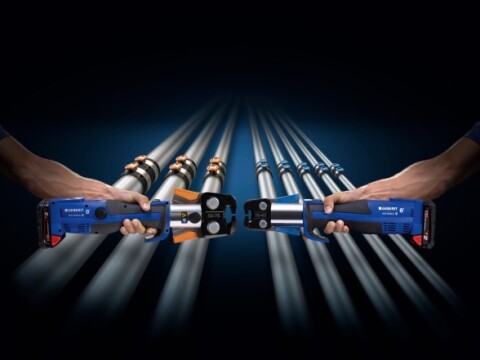 Zwei Hände, die elektrische Werkzeuge halten, mit mehreren Rohren im Hintergrund und einem dunklen, kontrastreichen Hintergrund.