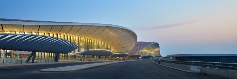 Modern airport terminal building with curved architecture against a twilight sky.