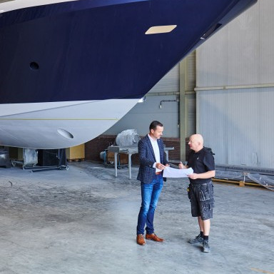 Zwei Männer mit einem Plan stehen in einer Werft vor einem grossen Boot.