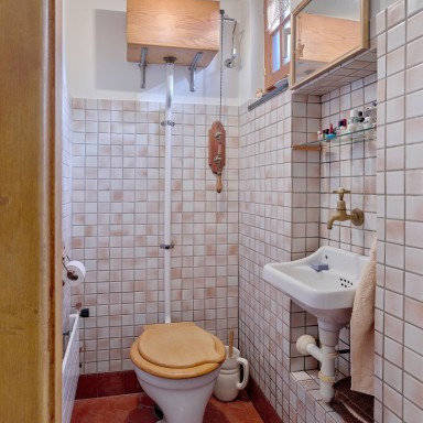 A small bathroom featuring a wooden toilet seat, a basin with a faucet, and tiled walls.
