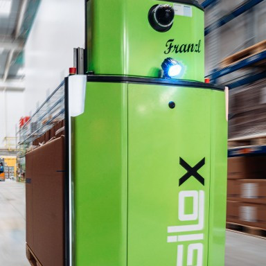 A green autonomous mobile robot designed for material handling in a warehouse environment.