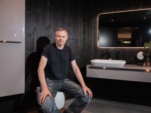 Ein Mann sitzt auf einer geschlossenen Toilette in einem modern gestalteten Badezimmer mit eleganten Badezimmerausstattung.