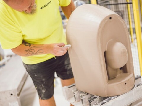 Ein Mann in einem leuchtend gelben T-Shirt arbeitet an einem grossen, ungefertigten Ton Objekt.