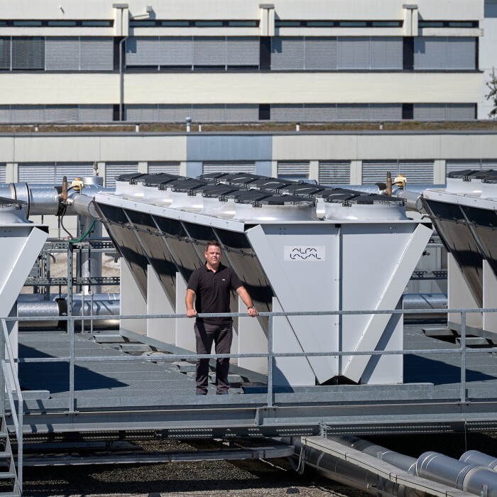 A person walking near large industrial cooling units on a rooftop, with a building in the background.
