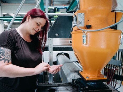 Eine Frau mit roten Haaren arbeitet an einer industriellen Maschine.