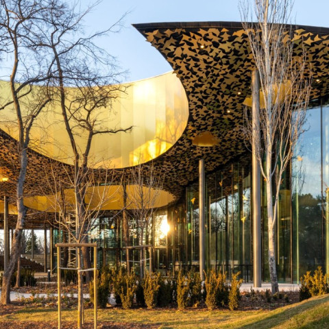 Moderne Architektur mit einem geschwungenen Dach, umgeben von Bäumen und Sträuchern.