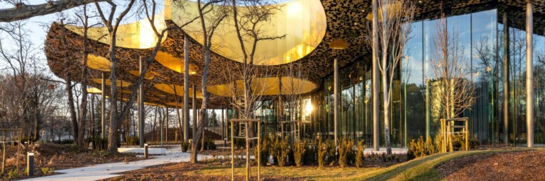 Moderne Architektur mit einem geschwungenen Dach, umgeben von Bäumen und Sträuchern.