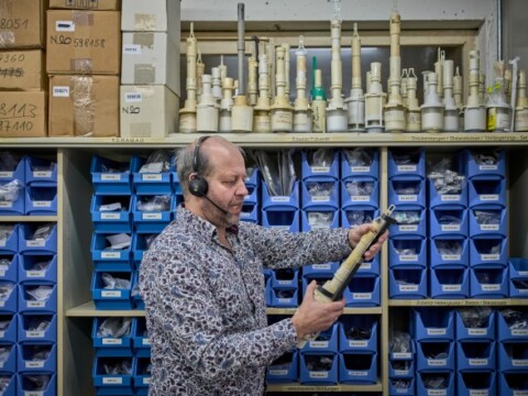 Ein Mann mit Headset betrachtet ein Spülventil in einem Lager mit blauen Aufbewahrungsboxen im Hintergrund.