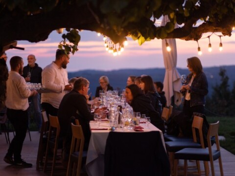 Eine Gruppe von Menschen sitzt an einem grossem Tisch im Freien, umgeben von einer warmen atmosphärischen Beleuchtung während des Sonnenuntergangs.