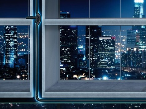A view of a city skyline at night through a modern window, and pipes visible in the walls.
