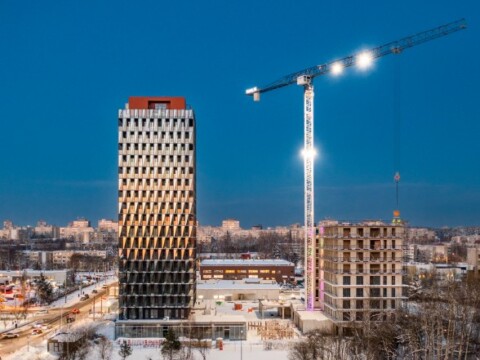 A winter construction site featuring two buildings, one fully built and one under construction, with a crane illuminated against a twilight sky.