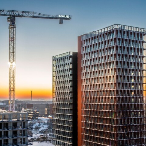 Construction site at sunset featuring two high-rise buildings and cranes against a colorful sky.