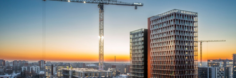 Construction site at sunset featuring two high-rise buildings and cranes against a colorful sky.