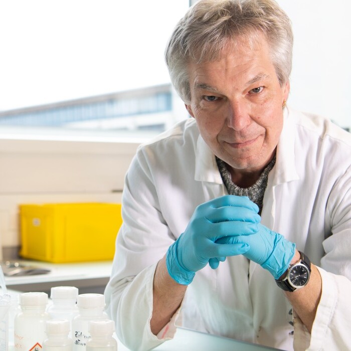 A man in a lab coat and blue gloves is working at a laboratory bench surrounded by various lab equipment and containers.