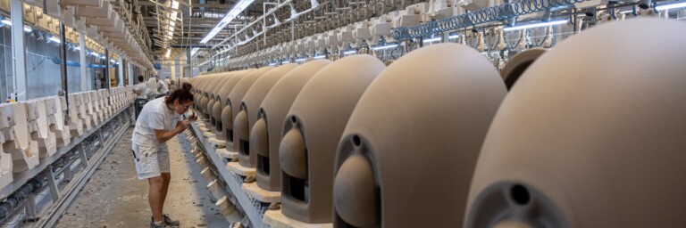 A production line in a factory featuring multiple beige ceramic pieces and workers.
