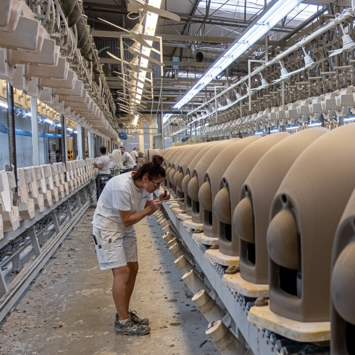 A production line in a factory featuring multiple beige ceramic pieces and workers.