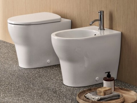 Ein modernes Badezimmer mit einem WC und einem Bidet, auf einem Steinboden vor einer Holzwand.