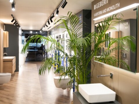 Innenansicht eines modernen Badezimmers mit Pflanzen, Waschbecken und Sanitäranlagen in einem Ausstellungsraum.