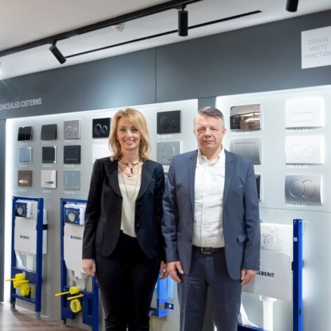 Zwei Personen stehen in einem Ausstellungsraum vor einer Wand mit Sanitärsystemen und Produkten der Marke Geberit.